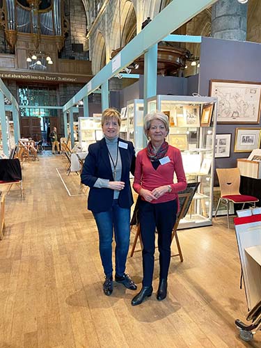 Impressie van de MABP 2025. Overzicht van het kerkinterieur met diverse stands. Op de foto Trudie Siegerink, penningmeester EW en Connie Stumpel voorzitter EW (links).